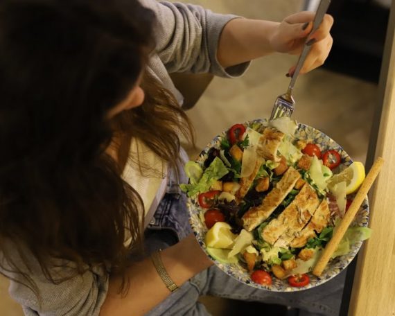 Overhead view of a woman eating a chicken salad balancing health with deliciousness.